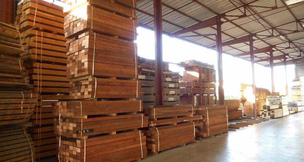 Des palettes en bois empilées dans un entrepôt au toit métallique, baigné d'une lumière vive.