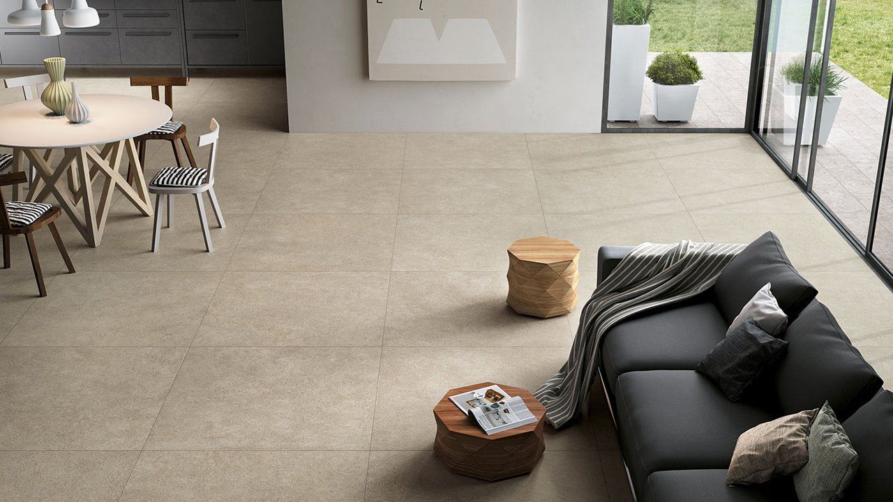 Salon moderne avec un canapé noir, des tables rondes et un sol carrelé beige près des portes coulissantes en verre