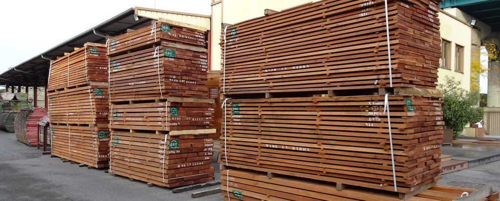 Des piles de palettes en bois sont entassées à l'extérieur d'une zone industrielle.