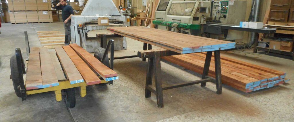 Deux remorques à plateau chargées de planches de bois dans un atelier industriel, un ouvrier se trouvant sur l'une d'elles en arrière-plan.