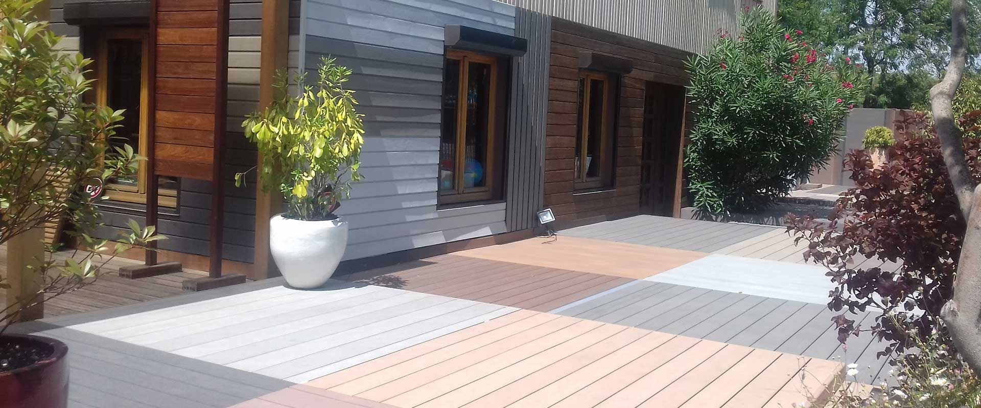 Terrasse moderne en bois avec allée carrelée, plantes en pot et façade d'un grand bâtiment vitré