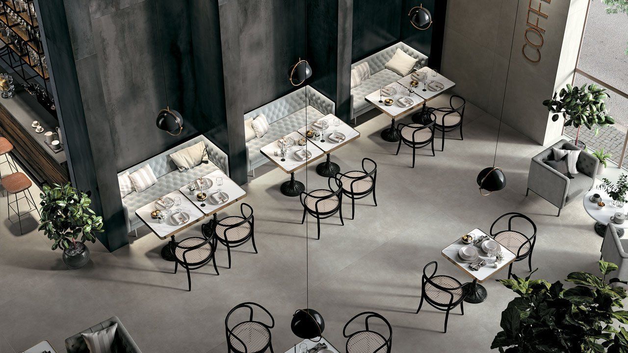 Vue aérienne d'un café moderne en plein air avec des tables blanches, des chaises noires et des plantes éparses.
