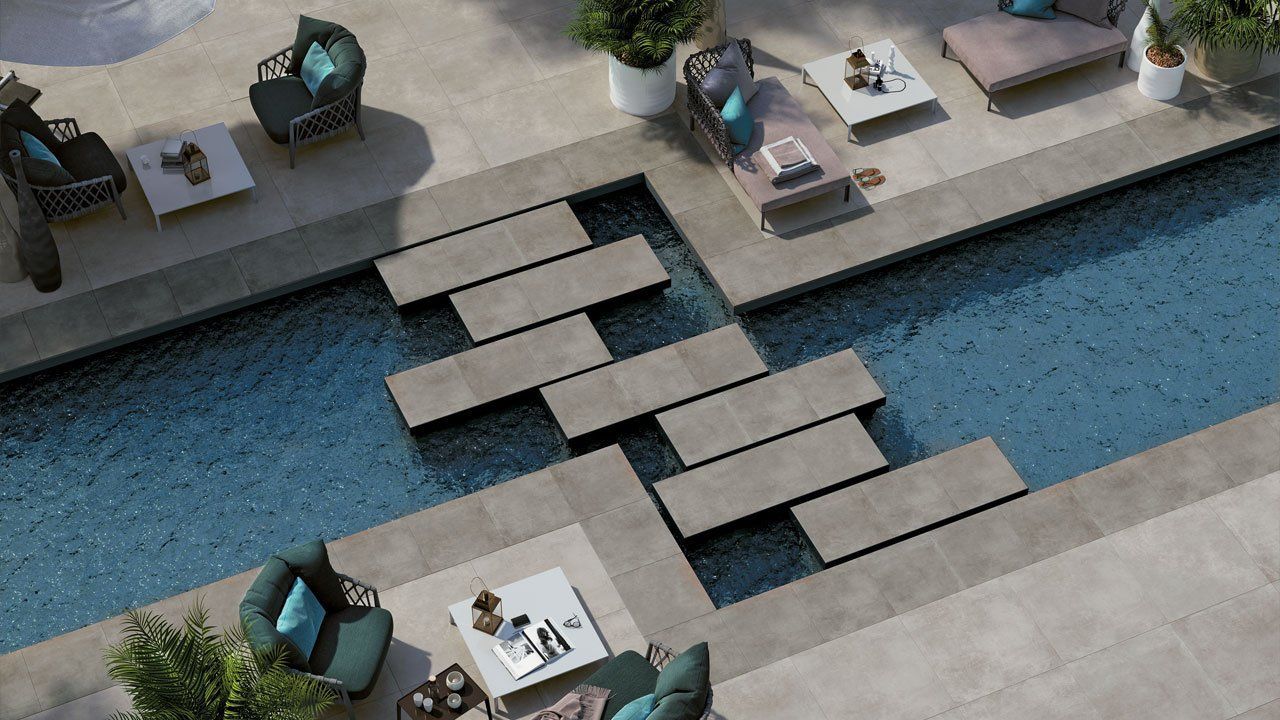 Vue plongeante d'un salon au bord de la piscine avec des dalles de pierre surplombant l'eau bleue et des chaises de patio avec tables.