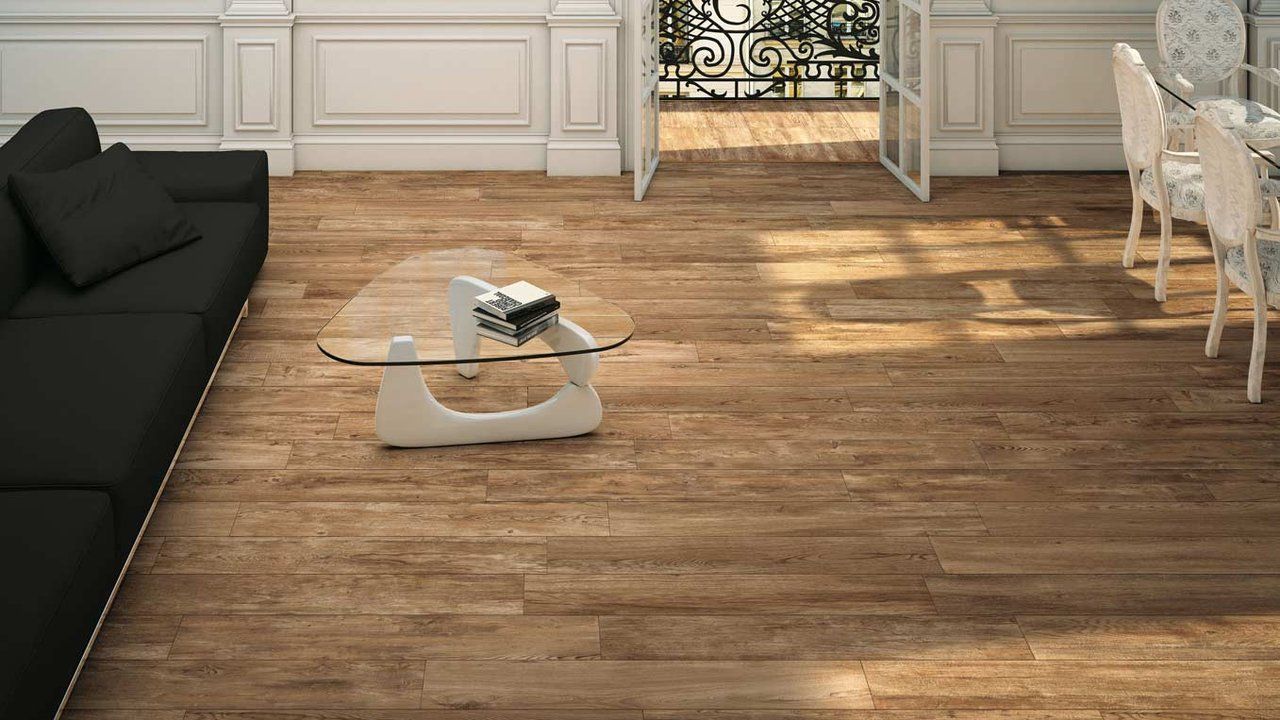 Salon moderne avec un canapé noir, une table basse en verre et un parquet baigné de lumière naturelle.