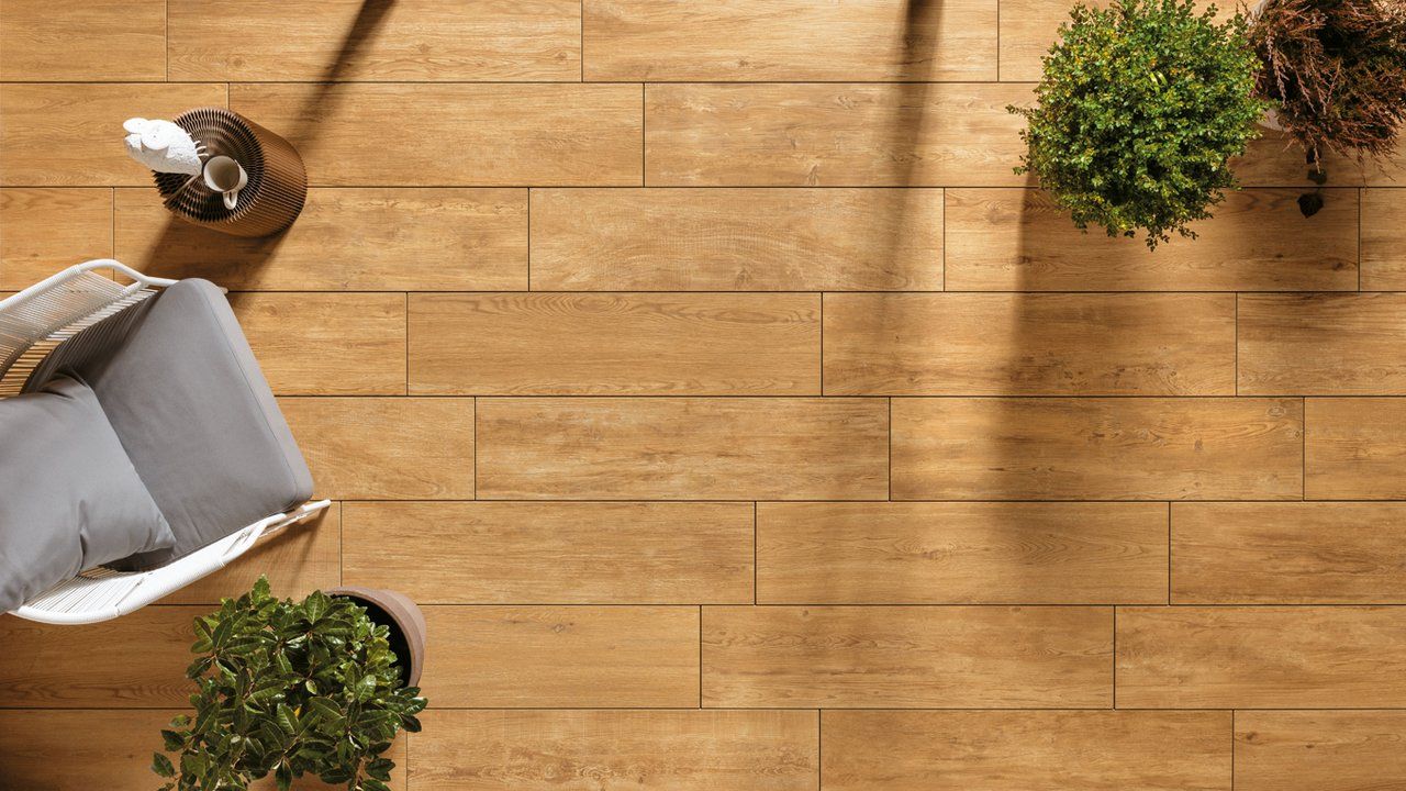 Vue plongeante d'une terrasse en bois ensoleillée avec une chaise, des plantes en pot et une petite table