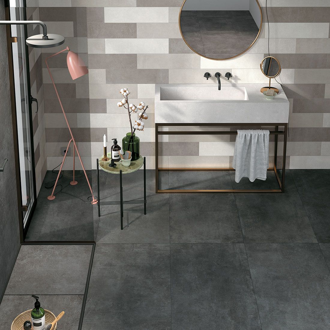 Salle de bain moderne avec carrelage gris, miroir rond, lavabo suspendu, douche et petit support pour plantes