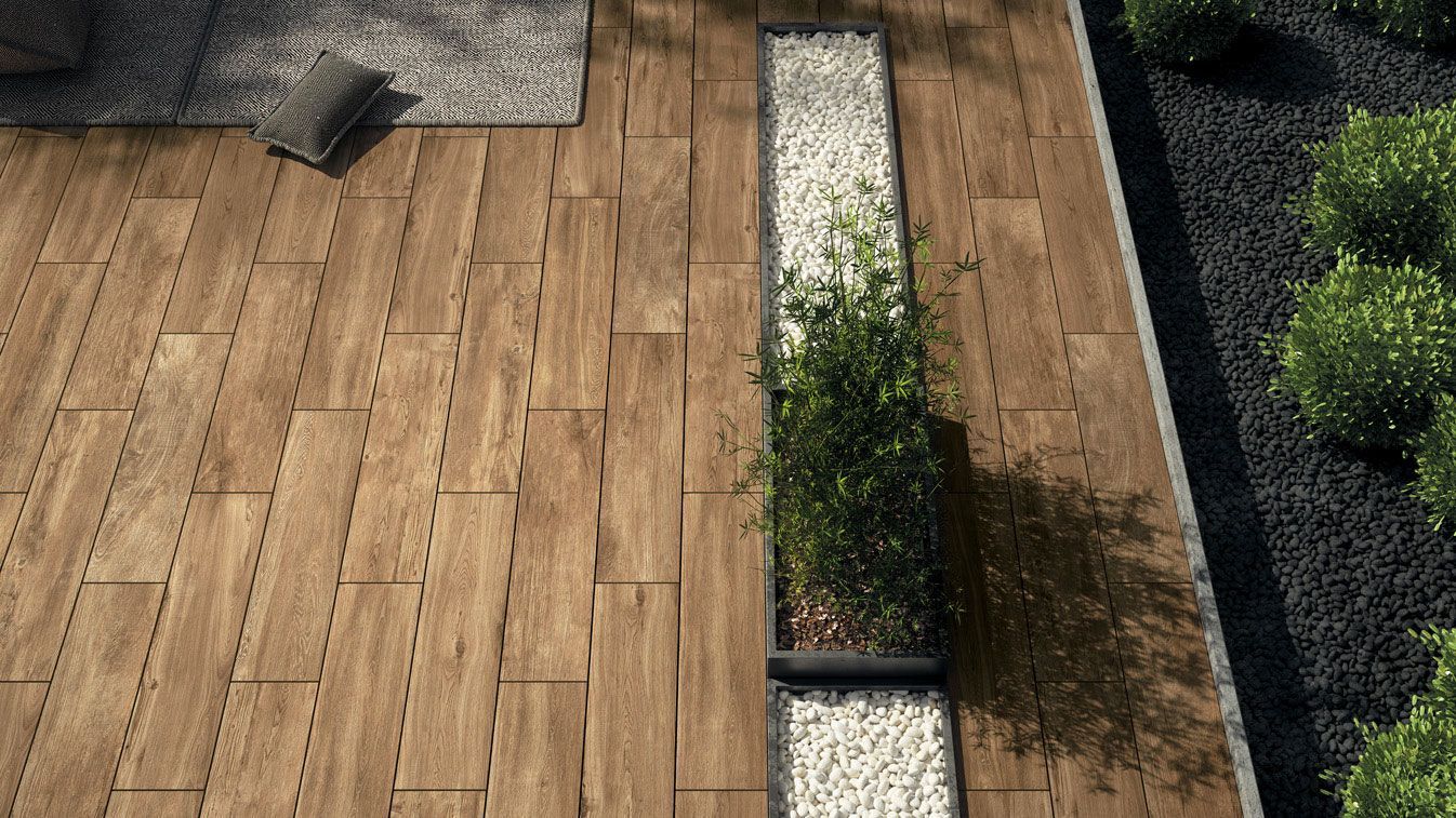 Terrasse en bois jouxtant une étroite bande de jardin bordée d'arbustes et de gravier.