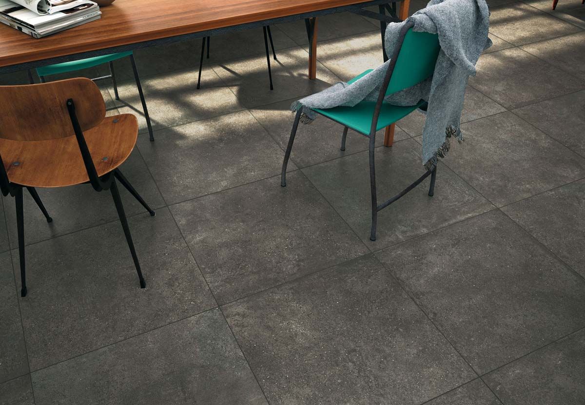 Salle de café vide avec sol carrelé noir, banc en bois et chaises turquoise et marron près d'une table