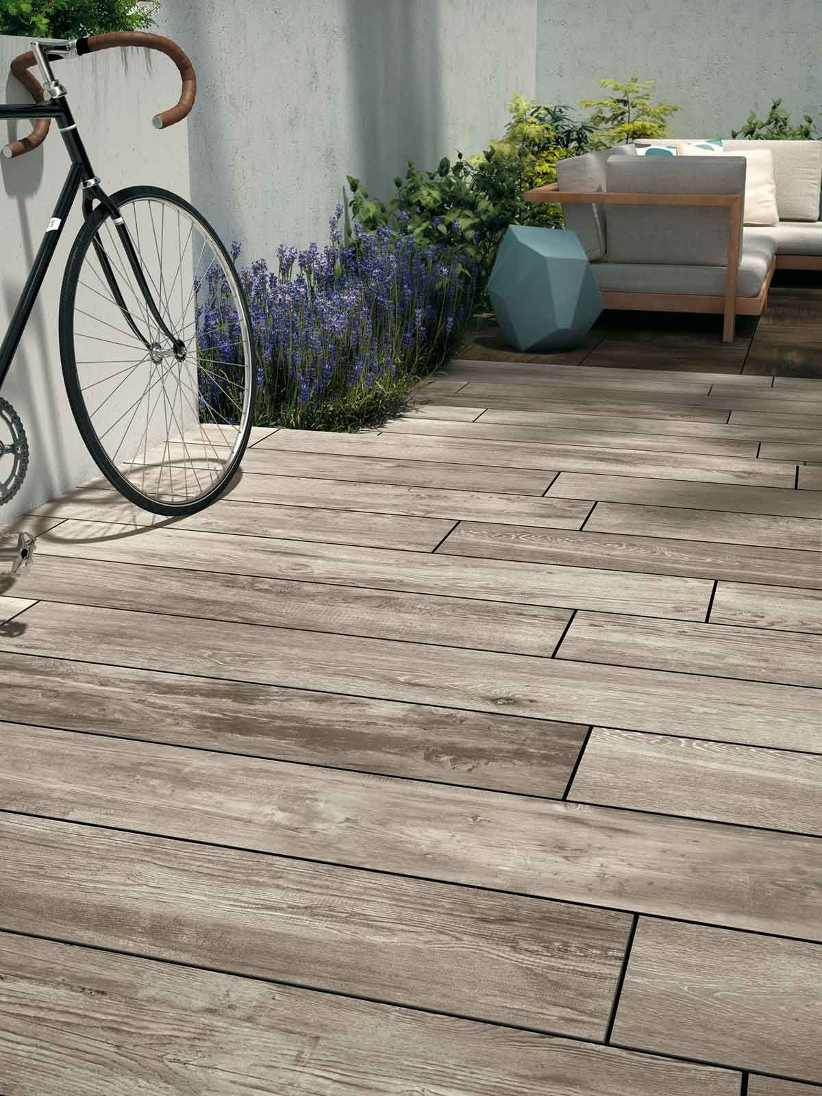 Terrasse ensoleillée avec un vélo, des fleurs en pot et une chaise contre un mur.