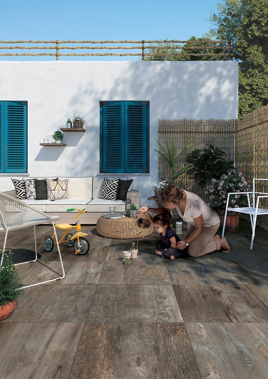Femme agenouillée avec un chien dans un patio ensoleillé, à côté d'une maison blanche aux volets bleus.