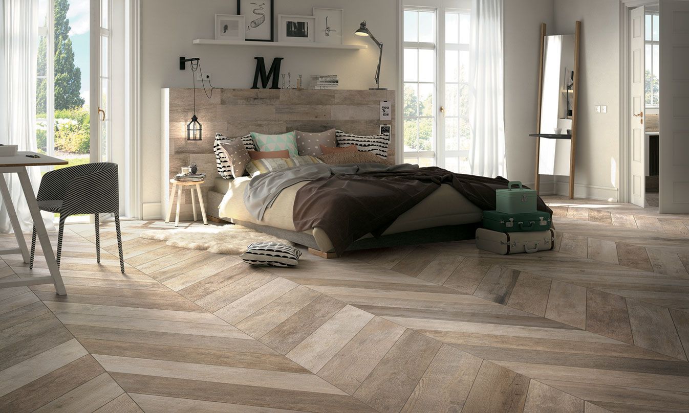 Chambre moderne et lumineuse avec lit, bureau, hautes fenêtres et parquet à chevrons