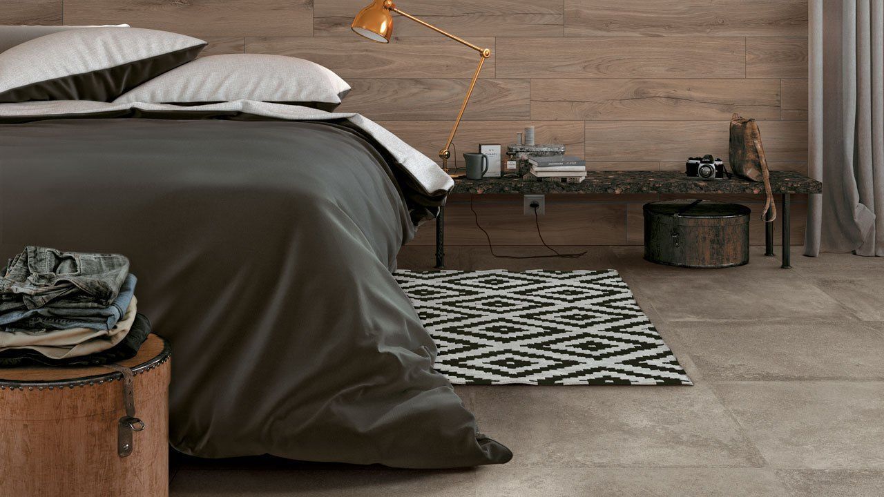 Chambre confortable avec un couvre-lit foncé, un tapis à motifs et un mur en bois rustique à côté d'une petite table