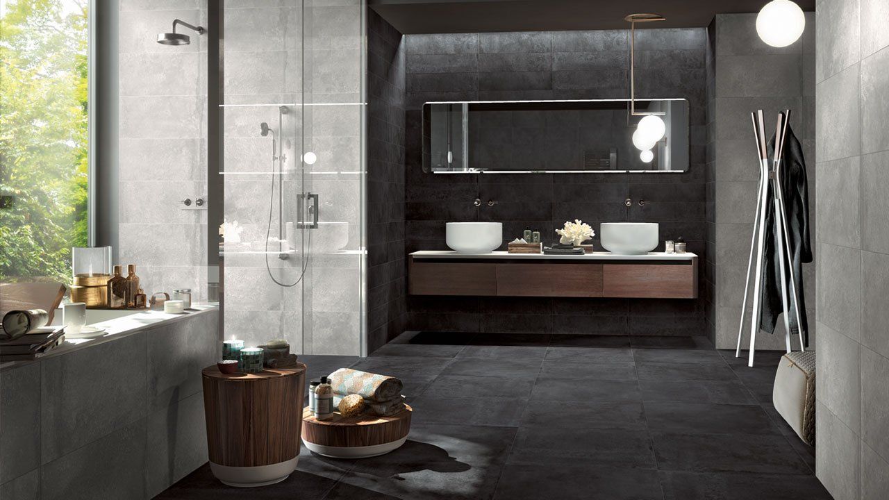 Salle de bains moderne et sombre avec murs en pierre, grand miroir, meuble-lavabo suspendu et baignoire îlot près d'une fenêtre