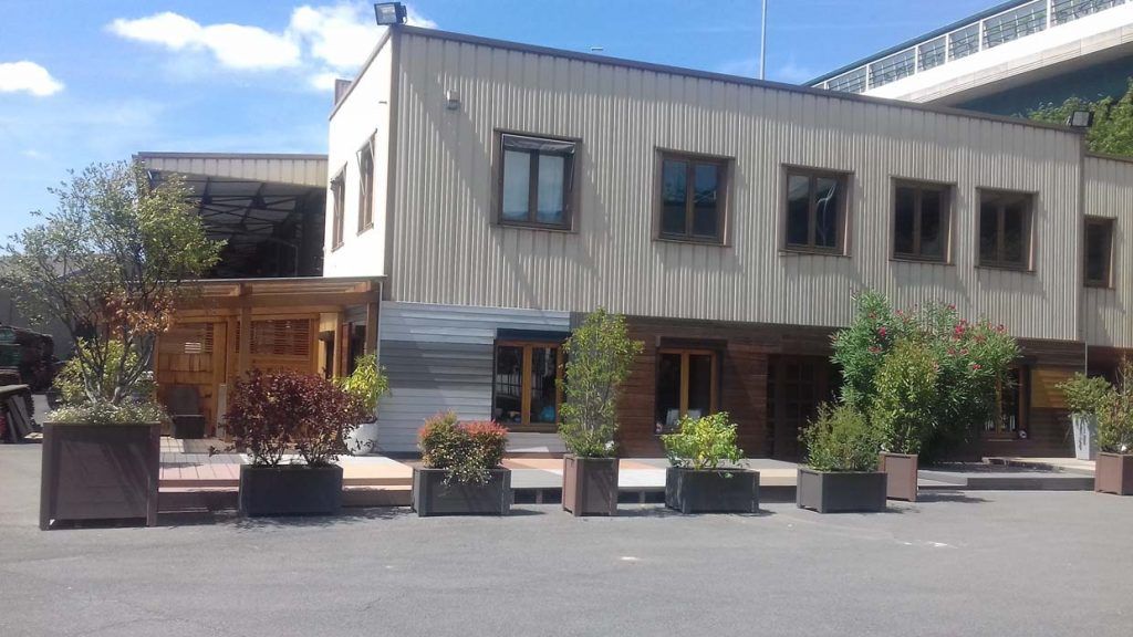 Bâtiment moderne avec fenêtres, plantes en pot et petite entrée en bois par une journée ensoleillée