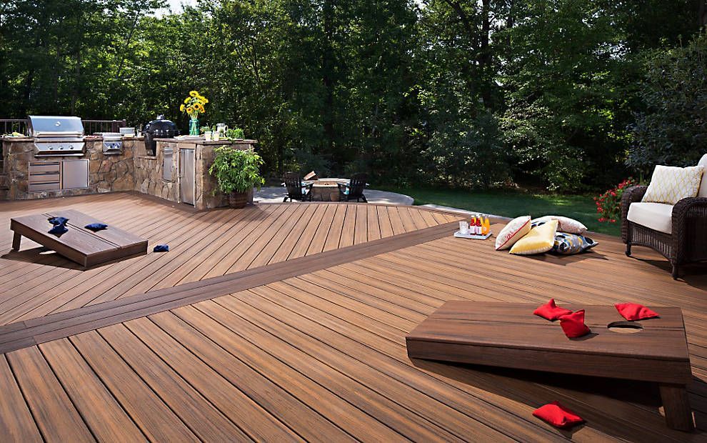 Terrasse en bois avec sièges d'extérieur, table et coussins épars donnant sur une zone boisée
