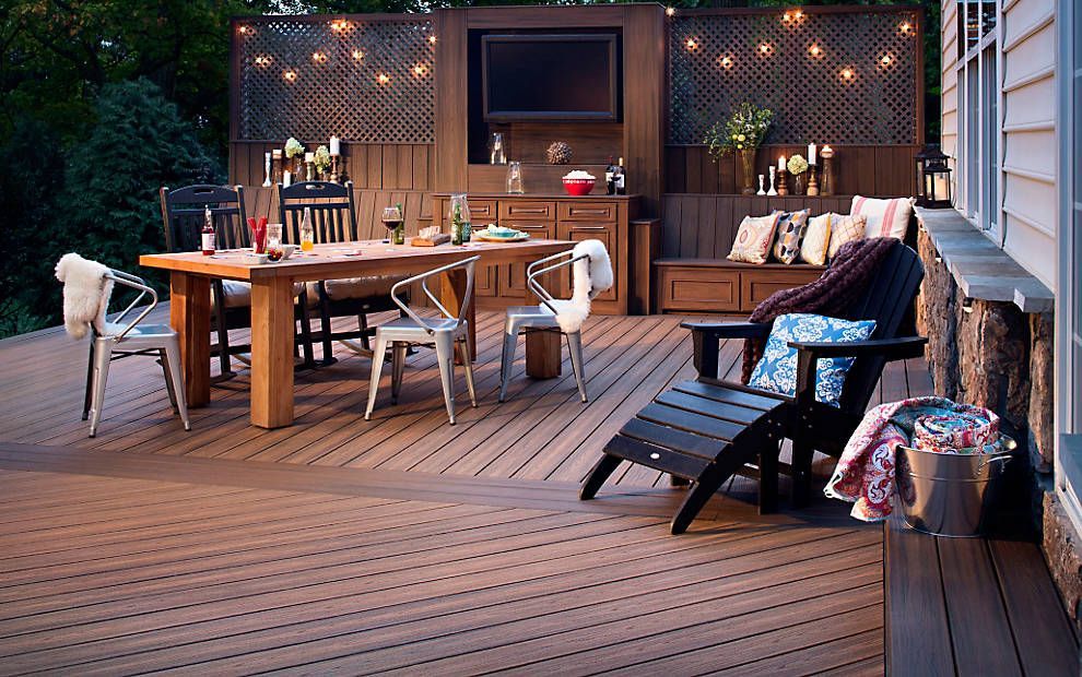 Terrasse arrière avec table à manger en bois, chaises, guirlandes lumineuses et chaise longue au crépuscule