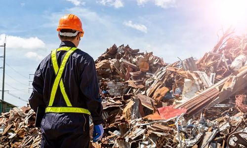 Un hombre con casco está parado frente a una pila de chatarra.
