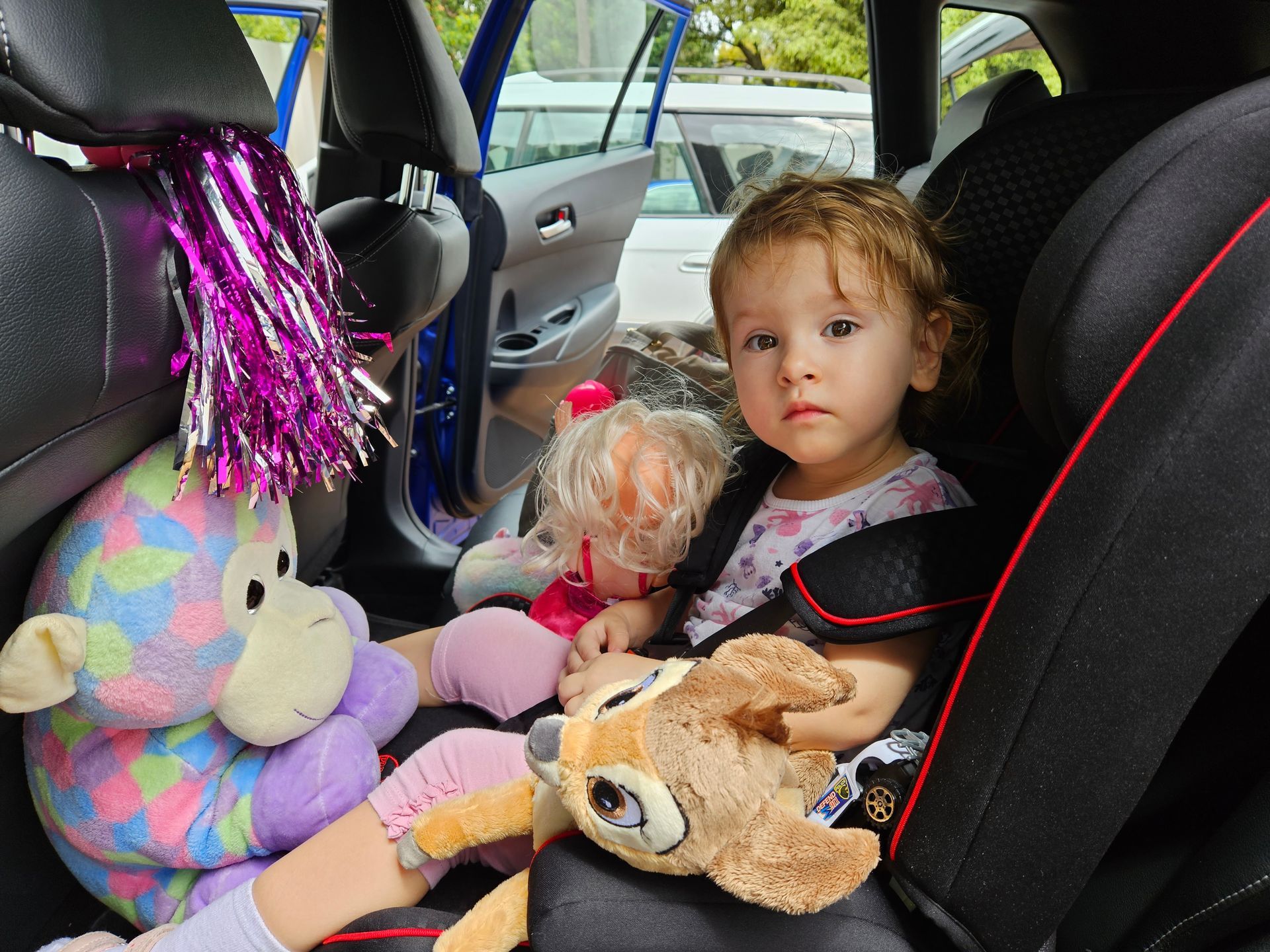 Un jeune enfant installé dans un siège auto, entouré de peluches, regarde l'objectif.