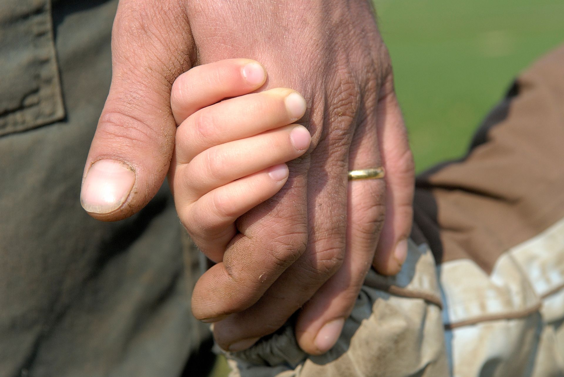 Une main d'adulte tient la main d'un petit enfant. L'adulte porte une bague.
