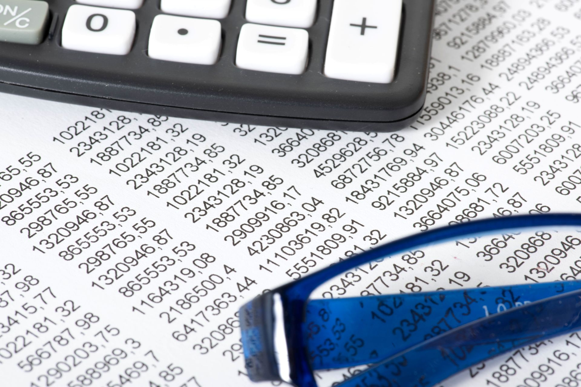 Calculatrice, lunettes et données financières sur une feuille imprimée.
