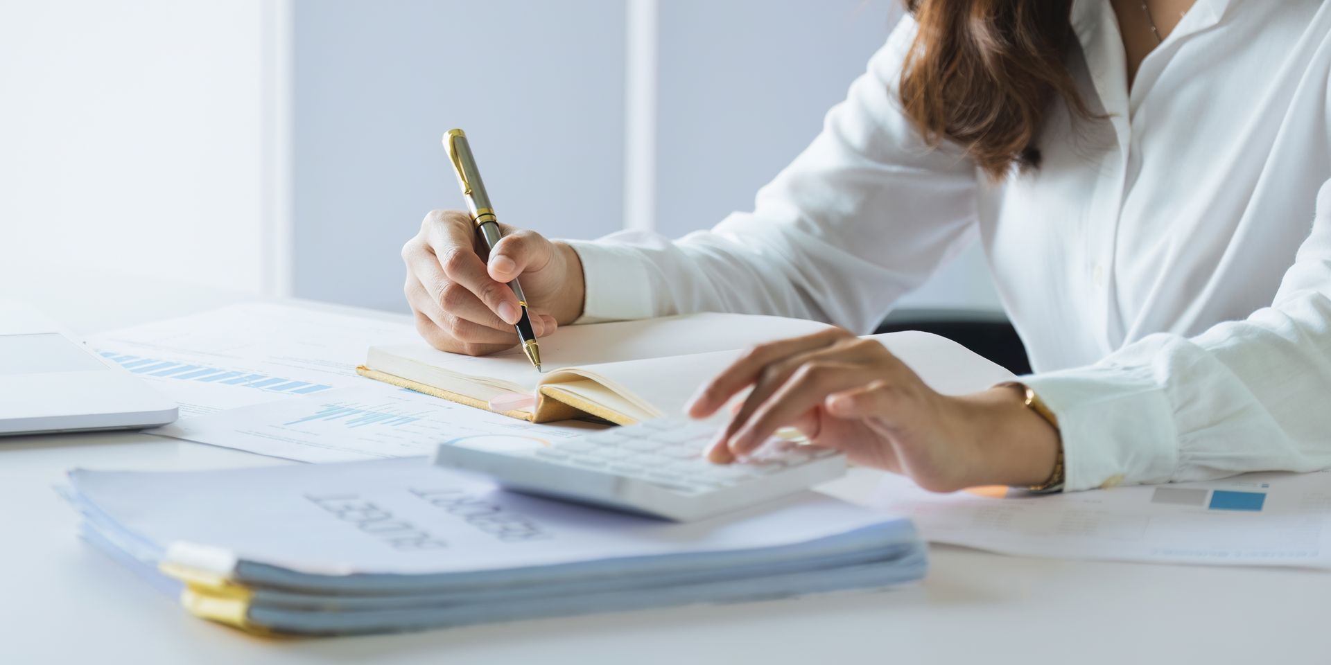 Une personne écrivant dans un cahier et utilisant une calculatrice à un bureau entouré de papiers.