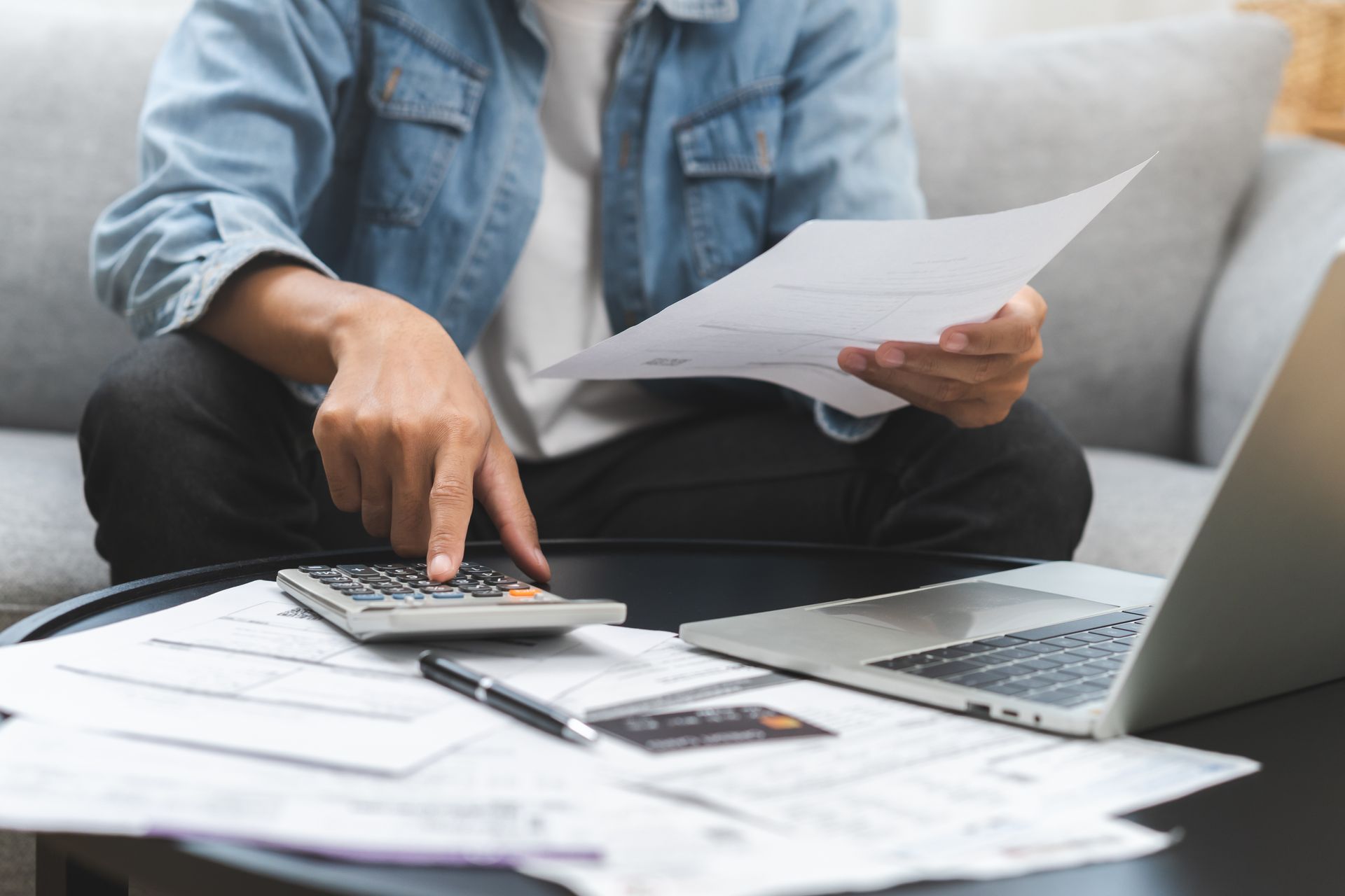 Personne calculant ses dépenses à domicile avec des papiers, une calculatrice, un ordinateur portable et une carte de crédit.