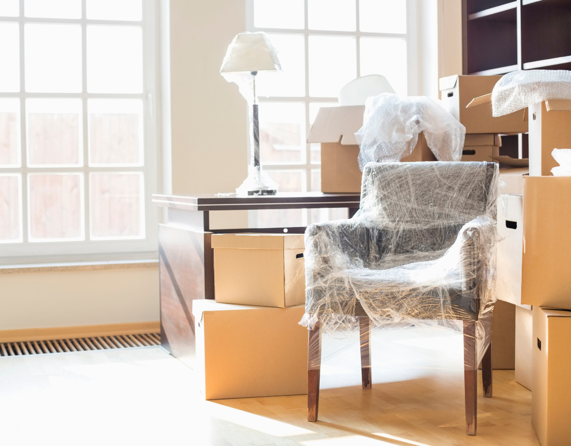 Une chaise enveloppée de plastique est posée dans une pièce entourée de cartons.