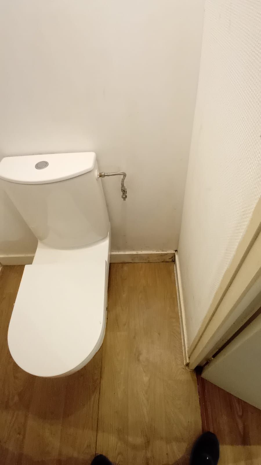 Des toilettes blanches sont posées sur un plancher en bois dans une salle de bain à côté d'une porte.