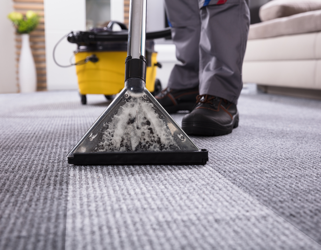 Une personne nettoie un tapis avec un aspirateur.