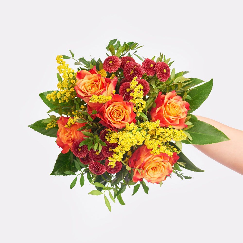 Bouquet of orange roses, yellow flowers, and red mums held by a person's hand.