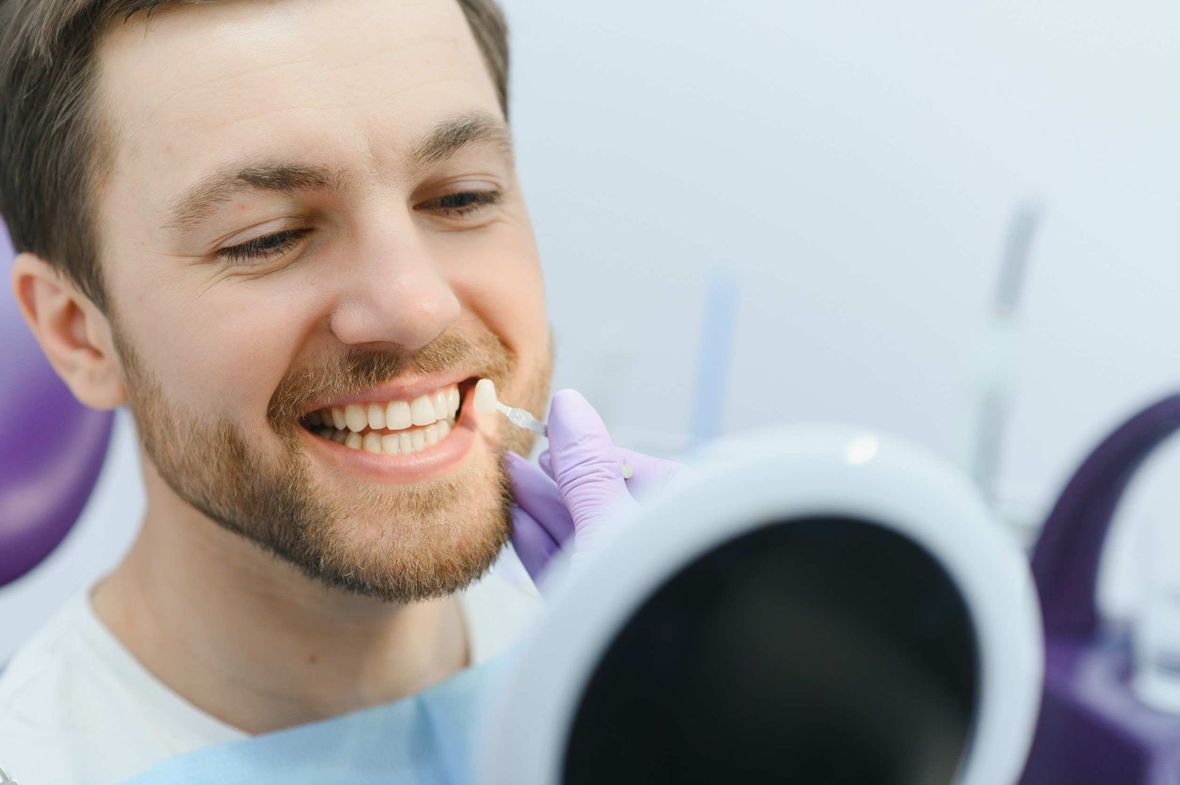 Un hombre sonríe mientras mira sus dientes en un espejo.