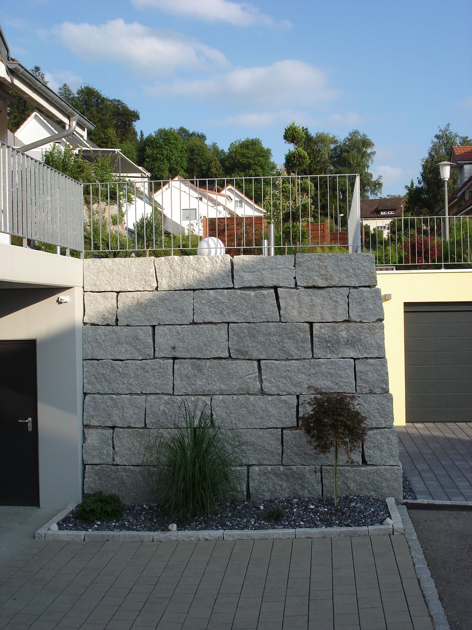 Eine große Steinmauer umgibt eine gemauerte Auffahrt vor einer Garage