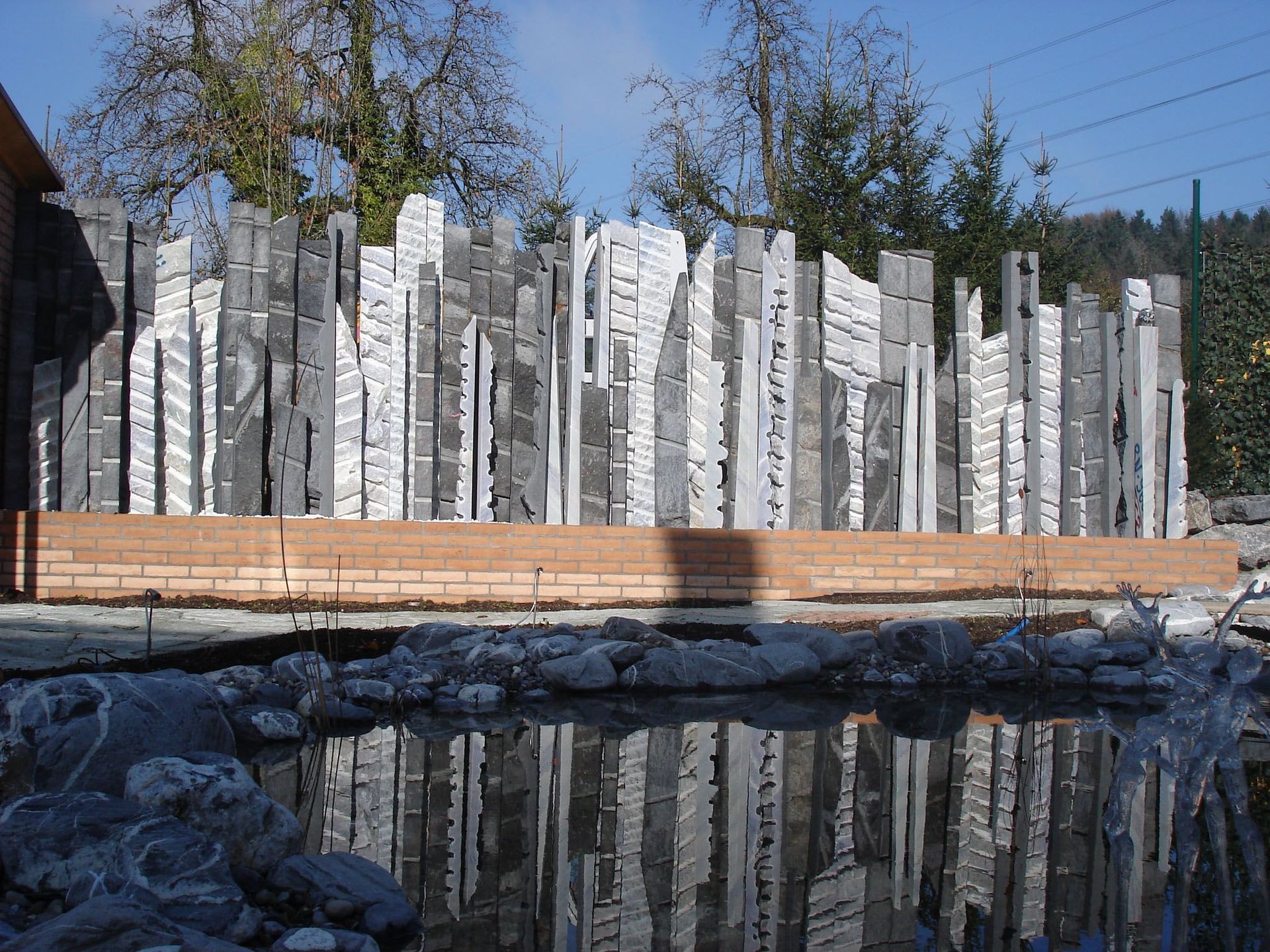 Ein Zaun aus Baumstämmen spiegelt sich in einem Teich