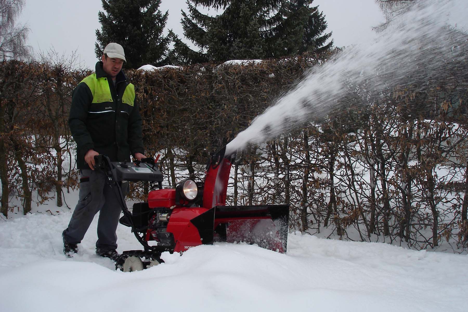 Ein Mann bläst Schnee aus einer roten Schneefräse