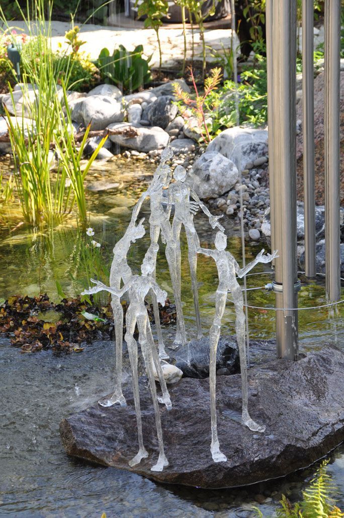 Eine Statue von drei Personen, die nebeneinander vor einem Teich stehen.