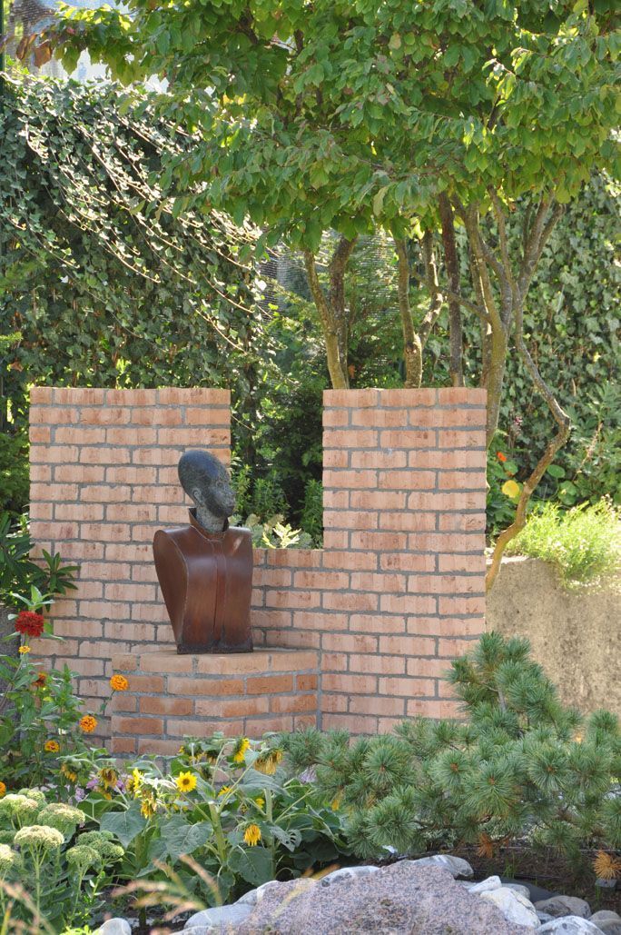 Eine Backsteinmauer mit einer Statue darauf in einem Garten.