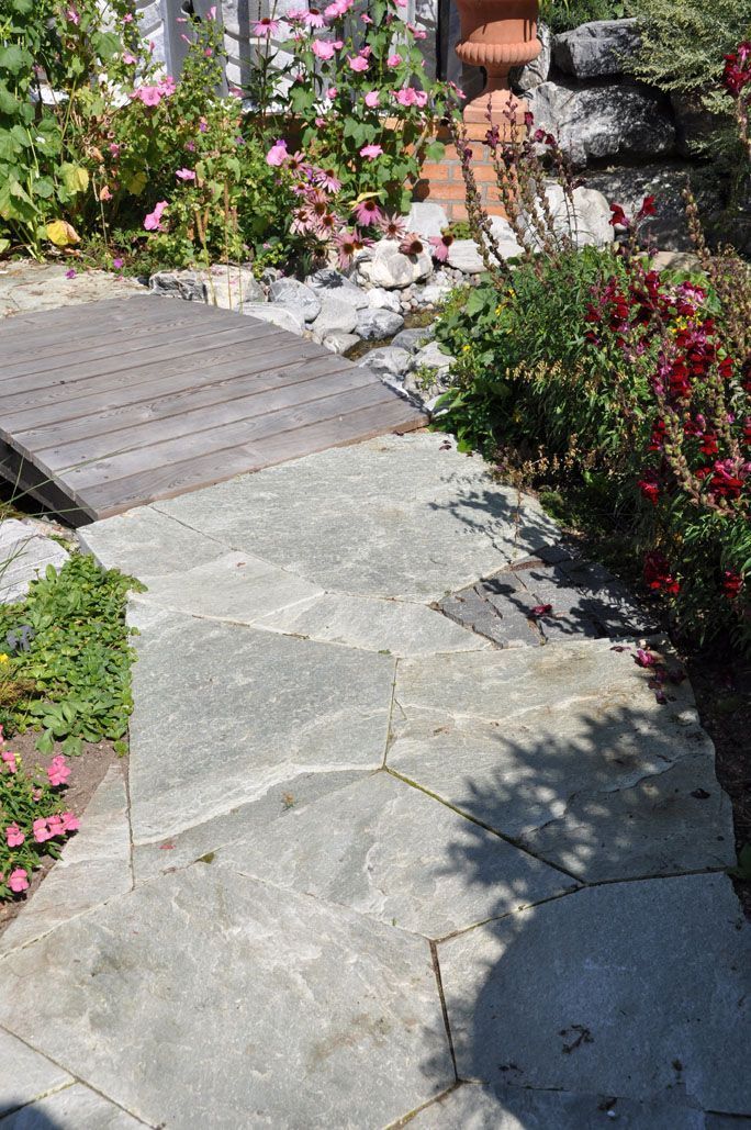 Ein Steinweg in einem Garten mit Blumen und einer Holzbrücke.