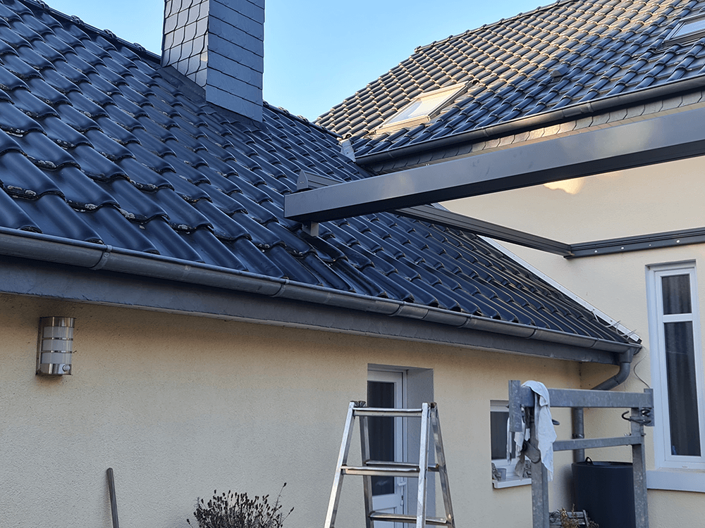 An der Seite eines Hauses neben einem Dach steht eine Leiter.