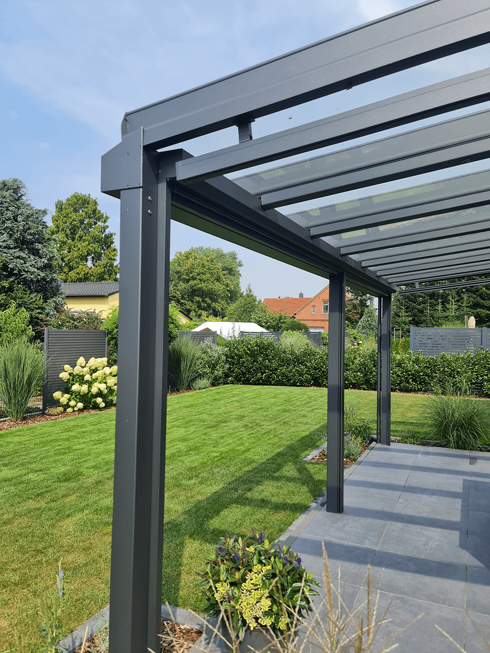Eine Pergola mit Glasdach steht inmitten eines Gartens.