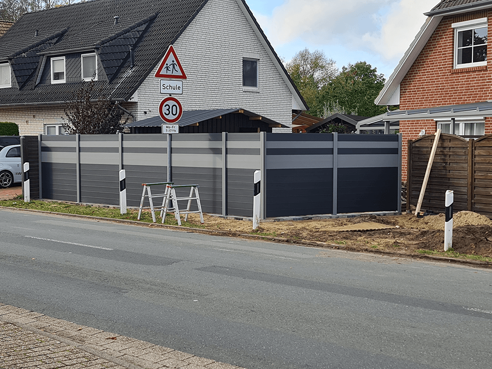 Ein Haus mit einem Zaun und einem Geschwindigkeitsbegrenzungsschild am Straßenrand.