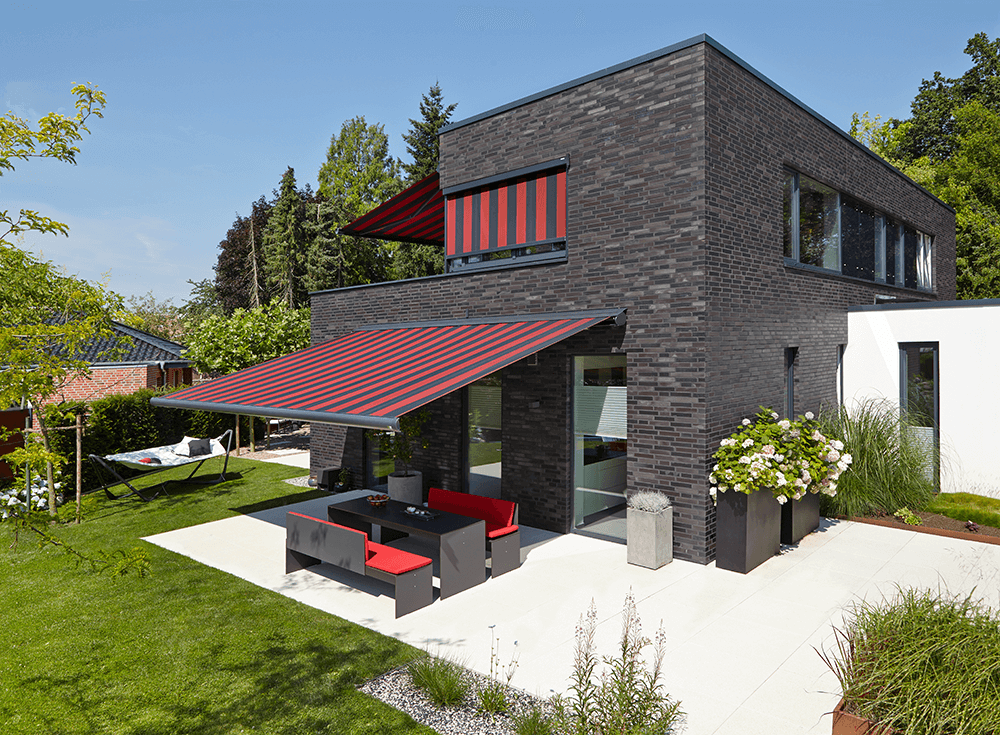 Ein Backsteinhaus mit einer roten Markise über der Terrasse.