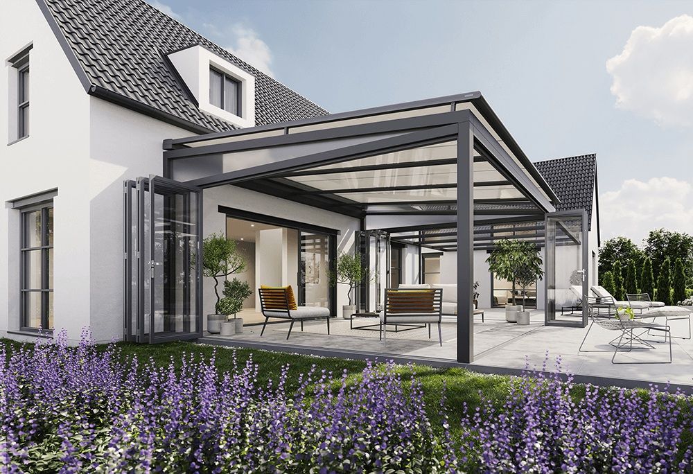 Ein weißes Haus mit einer Terrasse mit Baldachin und lila Blumen davor.