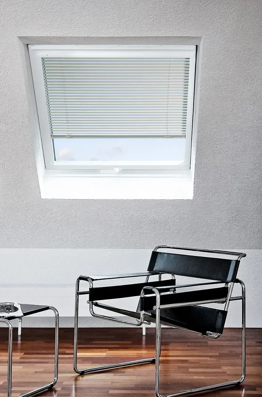 Ein schwarzer Stuhl steht vor einem Fenster mit Jalousien.