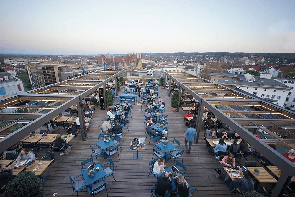 Eine Gruppe von Leuten sitzt an Tischen in einem Dachrestaurant.