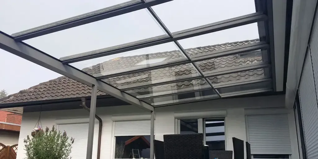 Eine Terrasse mit Glasdach und einem Tisch und Stühlen darunter.