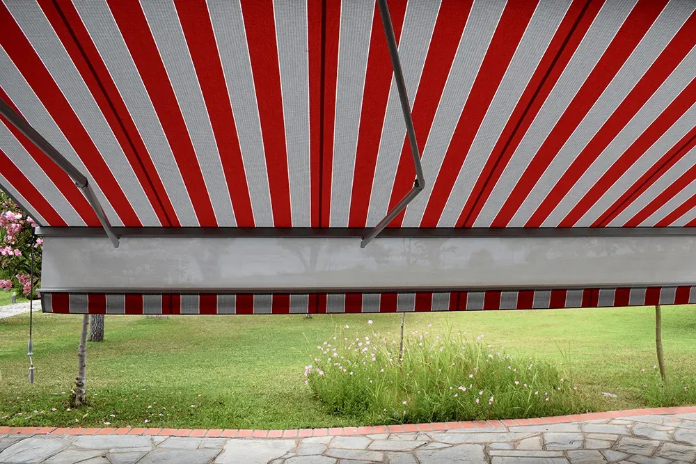 Eine rot-weiß gestreifte Markise hängt über einer Wiese.