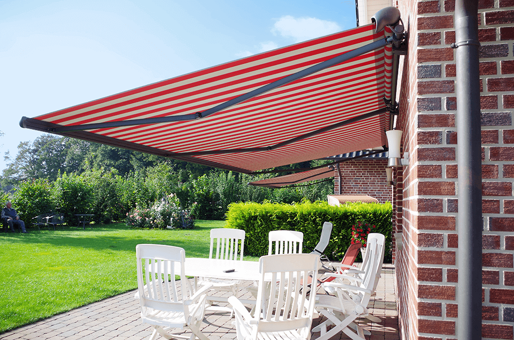 Eine rot-weiß gestreifte Markise überdacht eine Terrasse mit Tischen und Stühlen.