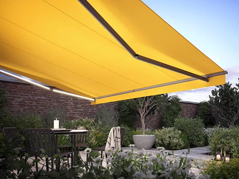 Eine gelbe Markise überdacht eine Terrasse mit einem Tisch und Stühlen darunter.