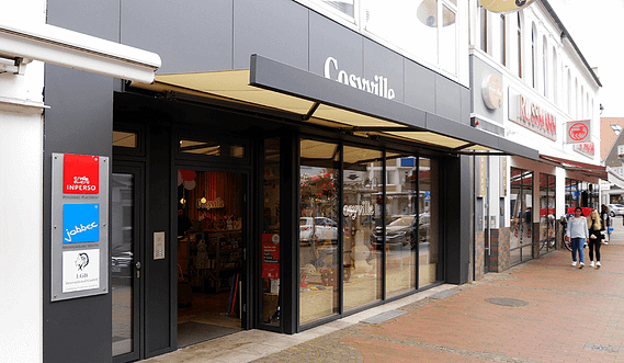 Eine Gruppe von Menschen geht einen Bürgersteig vor einem Geschäft entlang.