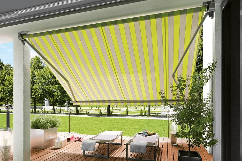 Eine Terrasse mit einer gelb-weiß gestreiften Markise darüber.